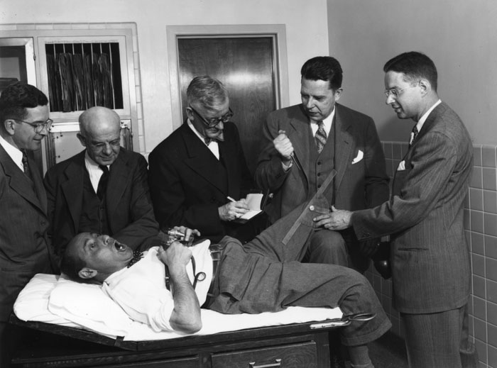 "When Life magazine sent the celebrated ALFRED EISENSTAEDT out to Mayo Clinic to photograph work on cortisone, Mayo consultants retaliated by throwing him on an examining table and subjecting him to cruel duress. At reader's left: Dr. CHARLES H. SLOCUMB; at his left: Dr. EDWARD C. KENDALL (1886-1972), who discovered and partially synthesized cortisone; center: Dr. JAMES ECKMAN; at his left: Dr. PHILIP S. HENCH (1896-1965), who introduced cortisone into the clinical practice of medicine; at his left: Dr. HOWARD F. POLLEY (applying protractor to determine mobility of joint). Dr. KENDALL and Dr. HENCH received the Nobel Prize in Physiology and Medicine in 1950 for their work on cortisone. Photograph taken at Saint Mary's Hospital, Rochester, Minnesota, on May 11, 1949, by ERVIN W. MILLER, Section of Photography of the Mayo Clinic, Rochester, Minnesota." [Philip S. Hench, MD Papers, MS076, McGovern Historical Center]