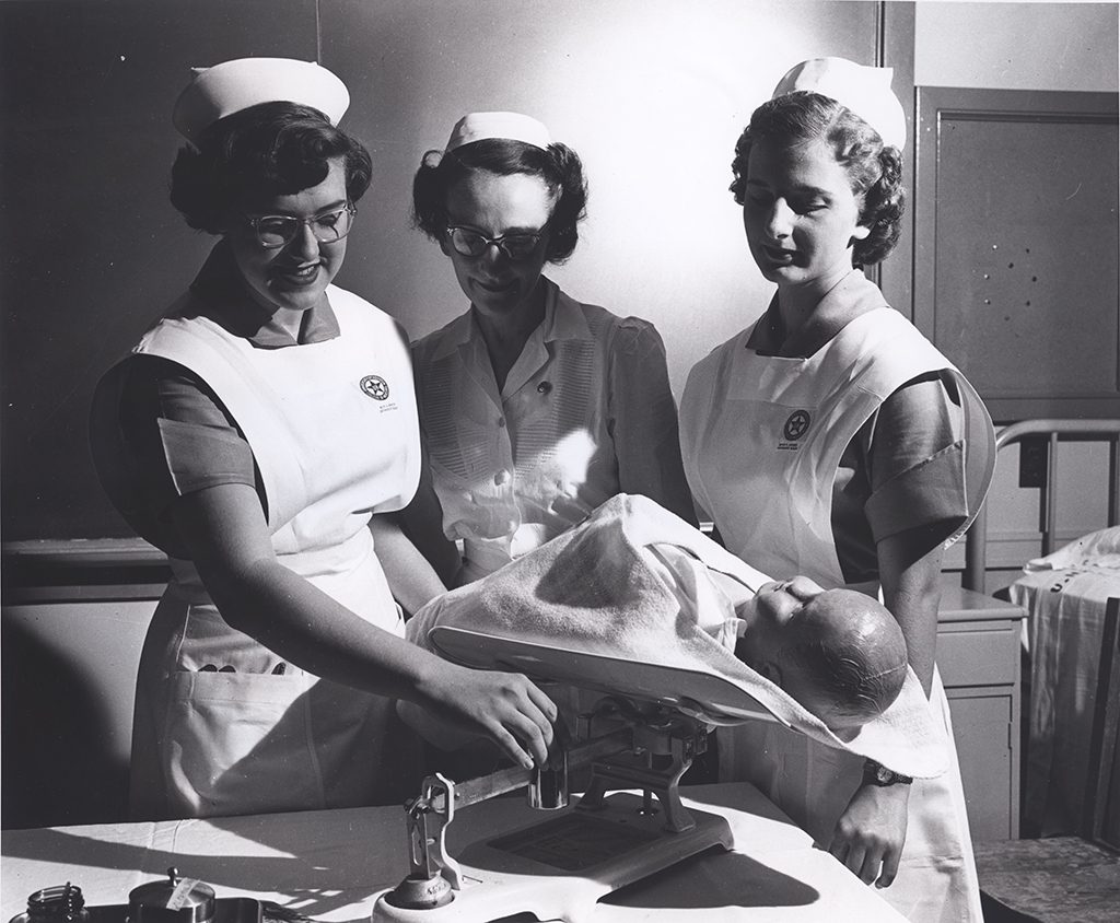 Photograph of nursing students and instructor weighing a baby doll at the University of Texas University of Houston, College of Nursing, 1952.