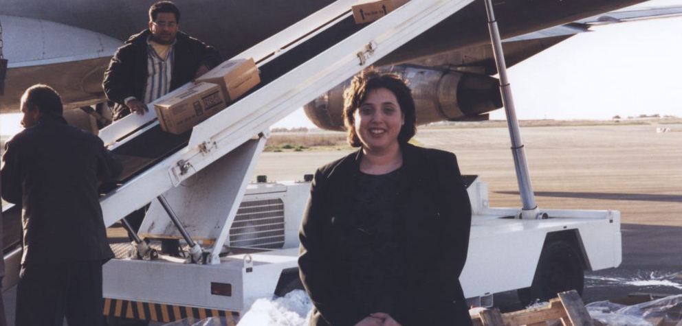 Cropped image of Debbie Goldberg, Executive Director of Texas Hadassah Medical Research Foundation, stands as medical supplies are unloaded from plane behind her at Yasser Arafat International Airport in Gaza on February 9, 1999. [IC 105 Texas Hadassah Medical Research Foundation records, McGovern Historical Center, TMC Library, IC105-024]